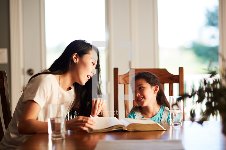 mother and daughter reading the Bible together at the kitchen table 
