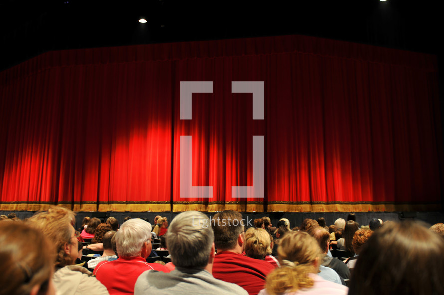 Audience facing a stage with curtains.
