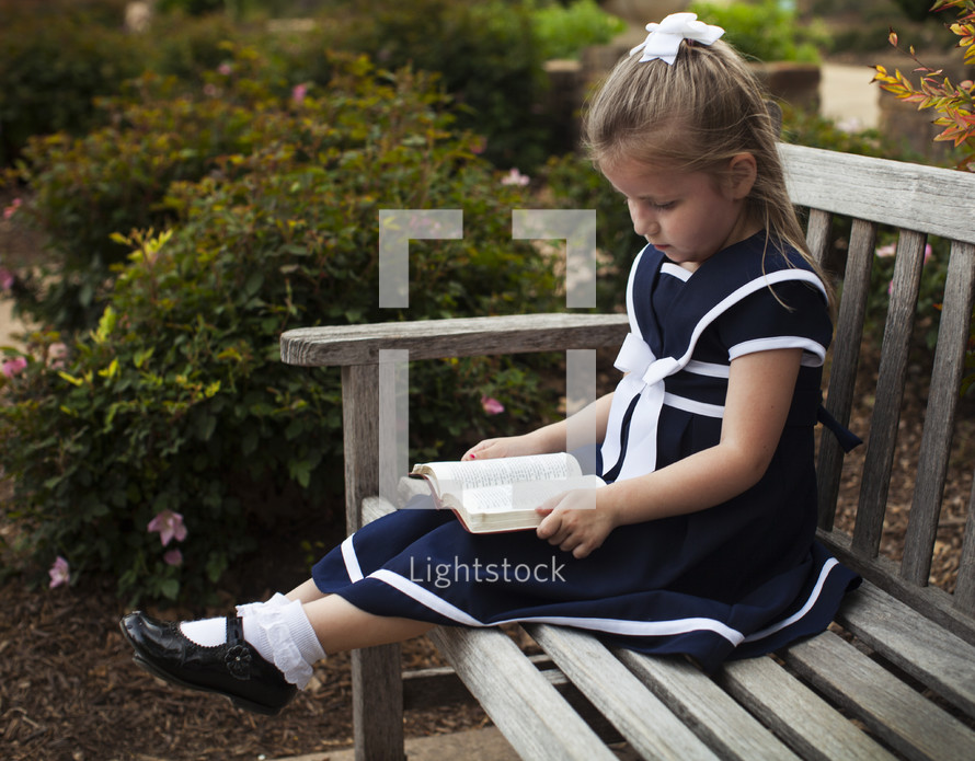 Girl sitting on a park bench reading the Bible.