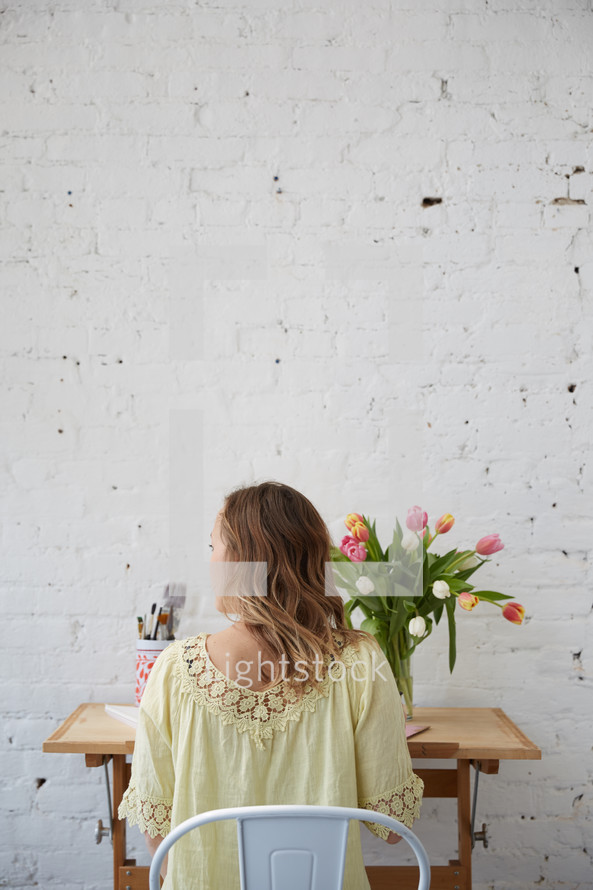 a woman sitting at a desk with spring tulips in a vase 