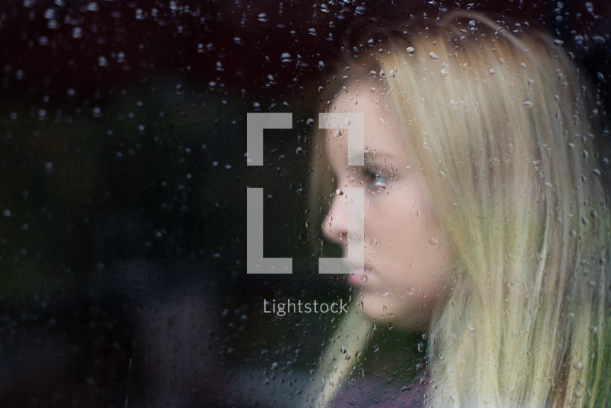 side profile of a woman's face through a rainy window 