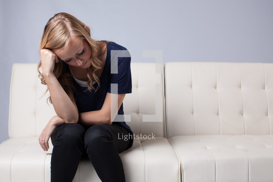 woman sitting on a white couch looking down 