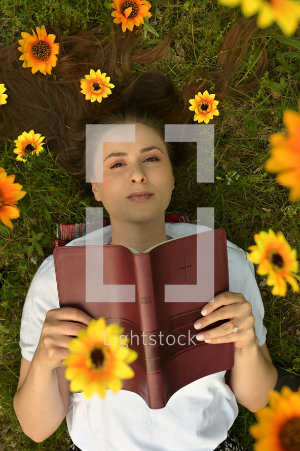 Portrait Of A Happy Girl With Flowers In Her Hair on Field holding a Bible 