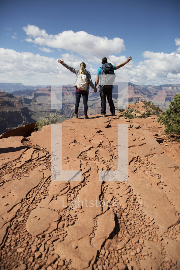 man and woman standing at the edge of a canyon cliff with raised arms 