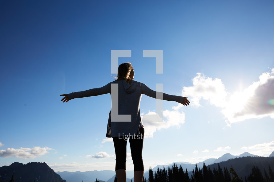 a woman with outstretched arms standing and taking in a mountain view 