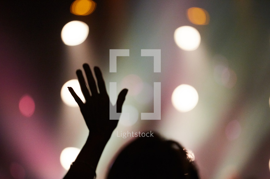 silhouette of a raised hand and bokeh lights 