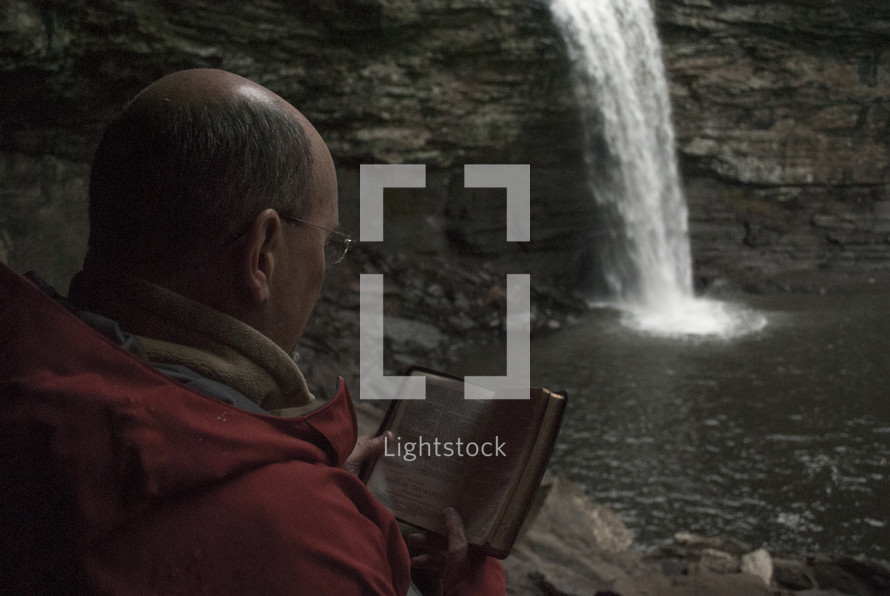 man reading a pocket Bible near a waterfall
