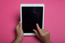Hands holding an electronic tablet, on a pink background.