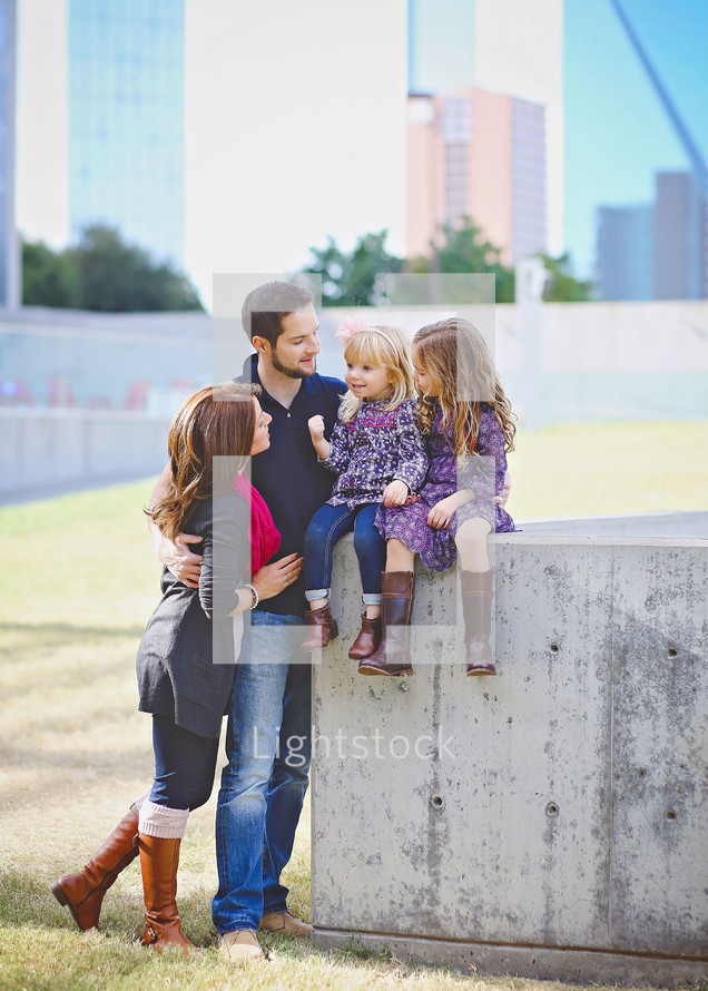family portrait with daughters sitting on a concrete wall 