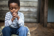 toddler boy sitting with praying hands 