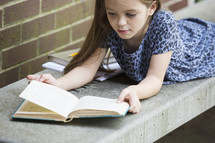 a child on a bench reading a book while waiting for school to start 