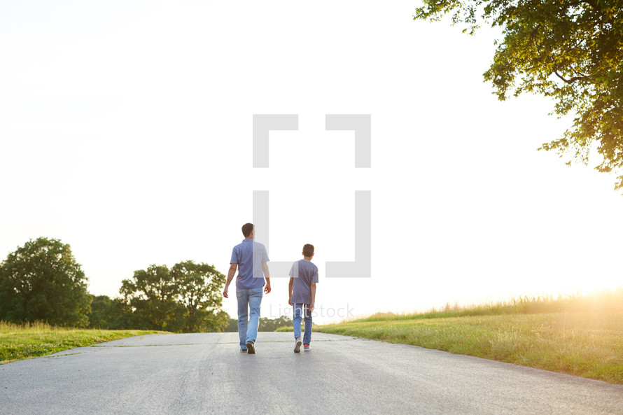 a father and son walking and talking down a rural road 