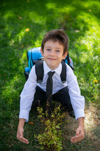 a child in dress clothes and a book bag hugging a tree 