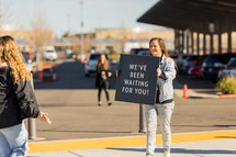 woman holding a We've been waiting for you sign in a church parking lot 