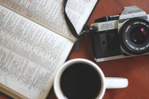 coffee mug, camera, and open Bible