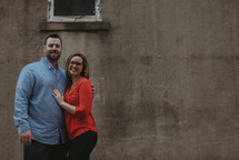 a couple standing together in front of a concrete wall 