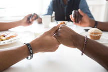 Group of men holding hands in prayer around a breakfast table.