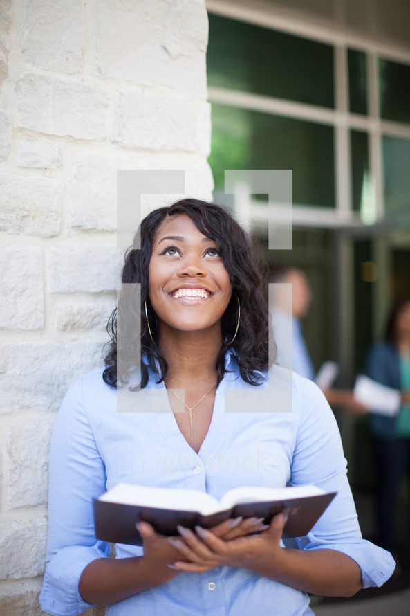 a smiling woman holding a Bible looking up to God 