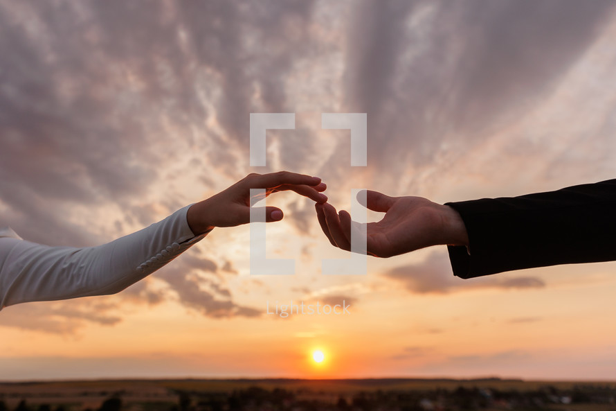 Hand of man and woman reaching to each other and touching on dramatic sunset sky background. Valentine day. Concept of human relation, community, togetherness, teamwork, love, symbolism