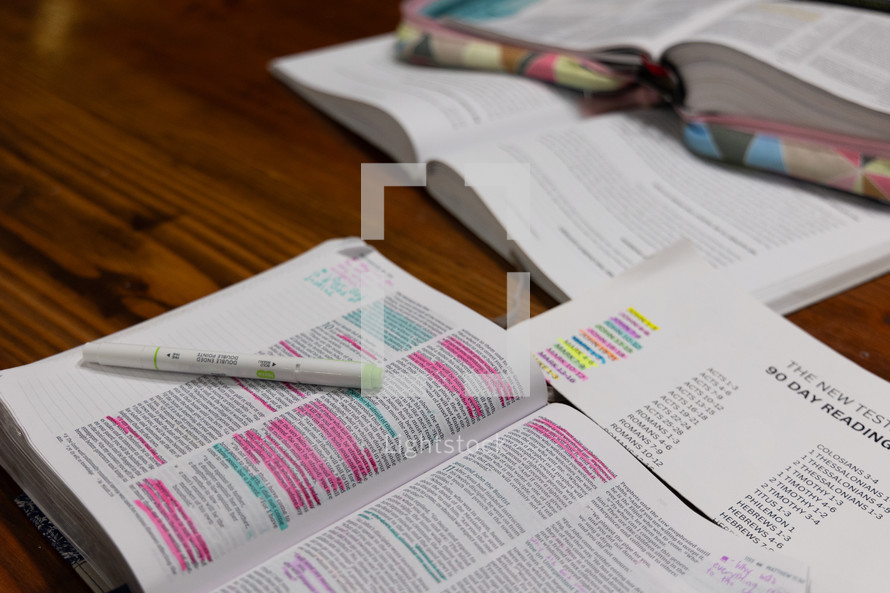 Open Bible with highlighted verses and highlighter next to New Testament reading plan paper and study book during women's Bible study