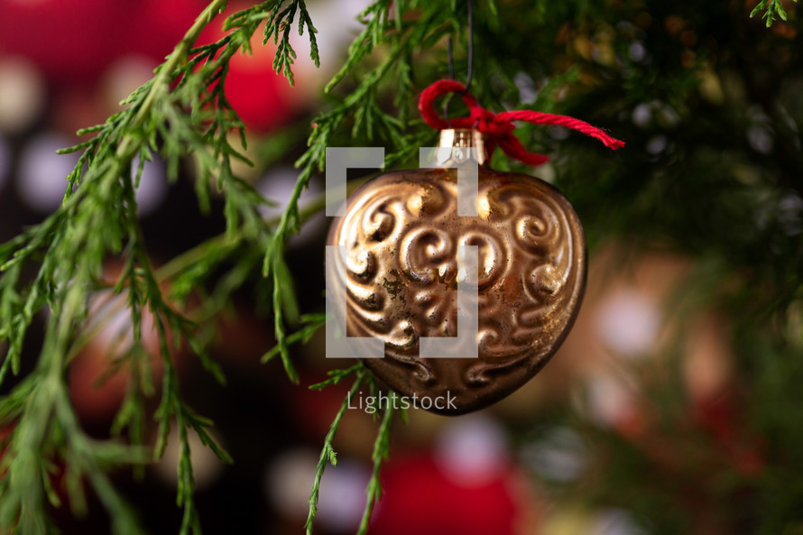 Gold Heart Ornament on the Branch of a Christmas Tree with Lights and Tree in the Background