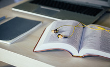 journal, earbuds on the pages of a Bible and a laptop computer on a desk 