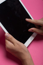 Hands holding an electronic tablet on a pink background.