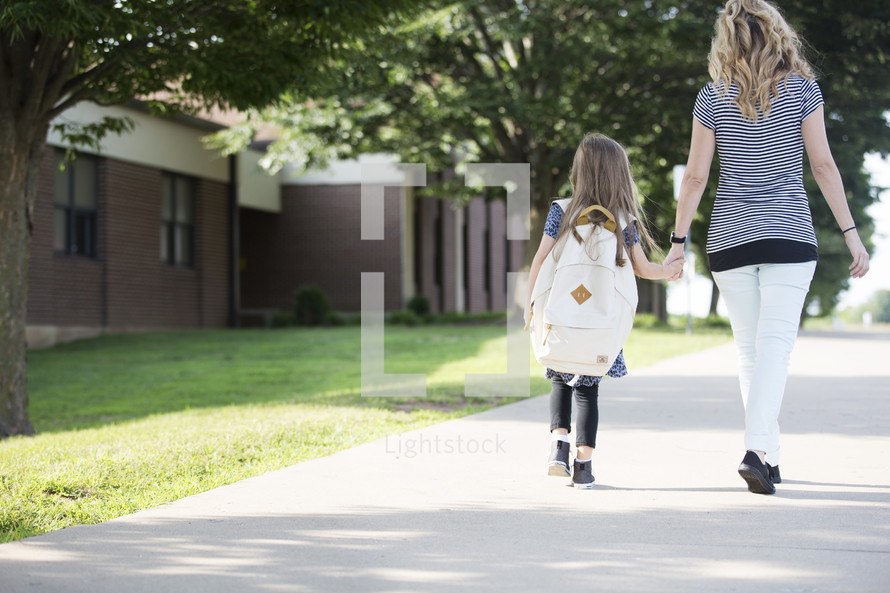 A mother and daughter holding hands and walking to school together.