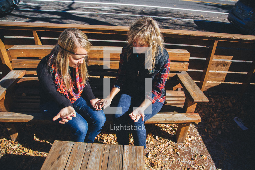 friends sitting outdoors on a bench holding hands in prayer 