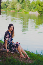 a woman in a floral dress sitting by a pond 