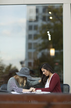 young women praying together at an outdoor table. 