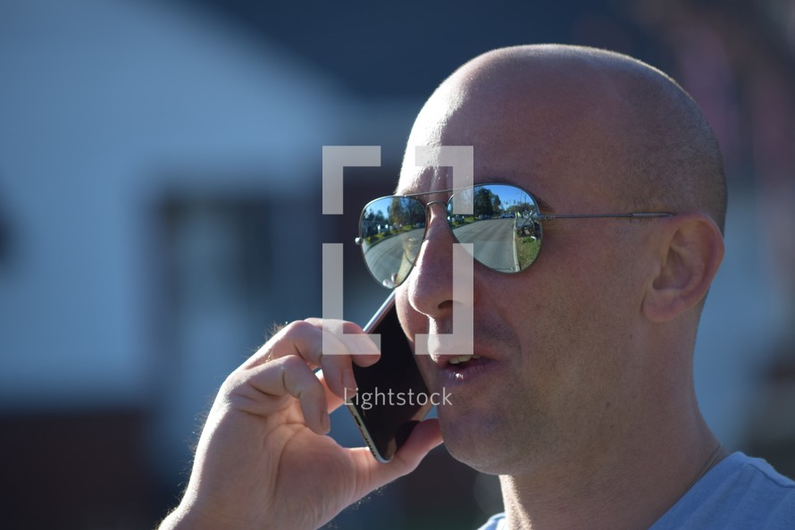 A man having a cellphone conversation with the reflection of the road ahead in his sunglasses 