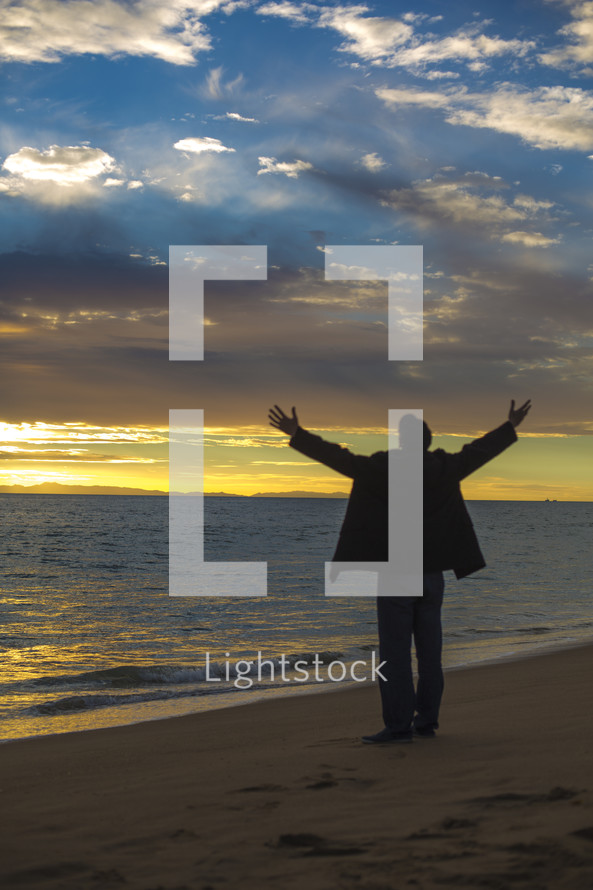 man with raised hands on a beach 