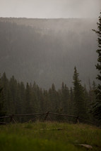 clouds and fog over a mountain forest and fence line 