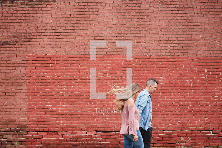 a couple walking holding hands in front of a red brick wall 