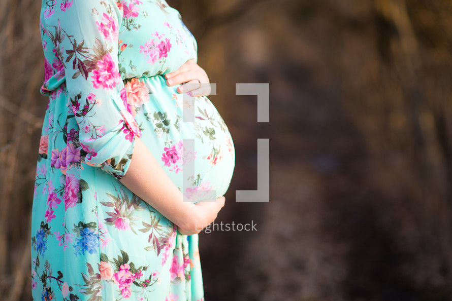 pregnant woman in a floral dress holding her belly 