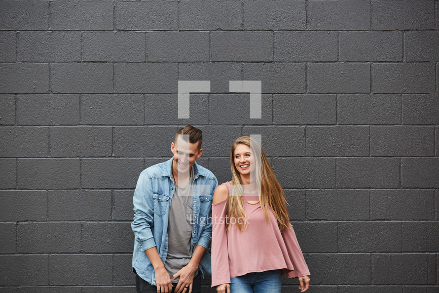 a couple standing in front of a gray wall 