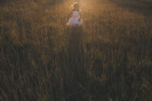 a girl child in a dress running through tall grass at sunset 