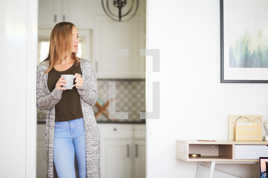 a woman with a coffee cup standing in a kitchen 