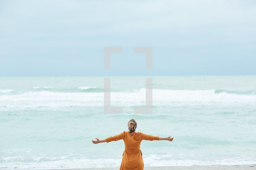 a woman standing on a beach with open arms 