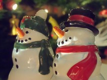 Two snowmen figures enjoy the Christmas festivity of lights, color, sounds and smells of Christmas that bring a smile to all who experience it as these two figures revel in the joy that is Christmas. 