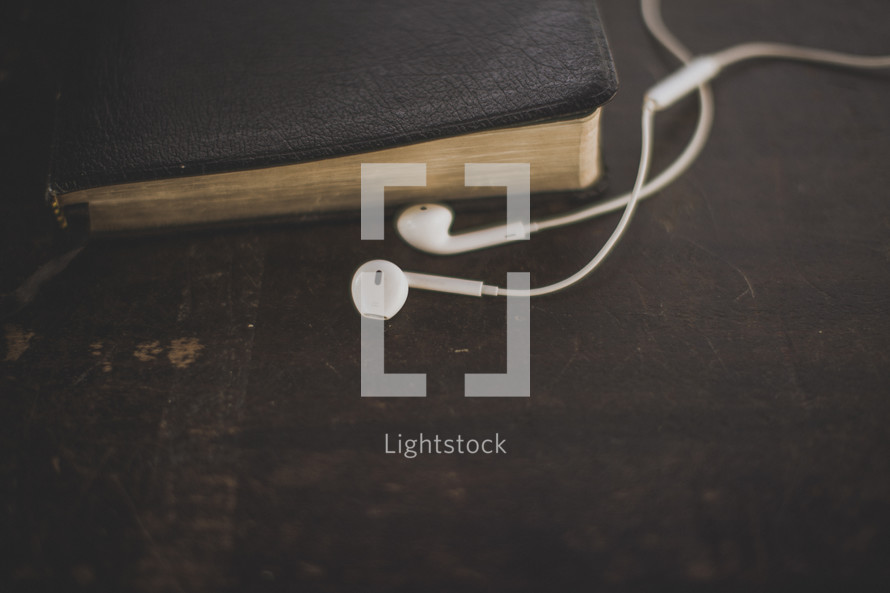 White ear buds and a Bible on wood