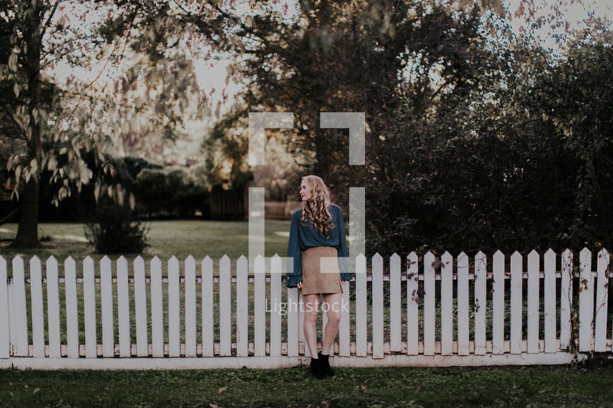 a young woman standing in front of a white picket fence 