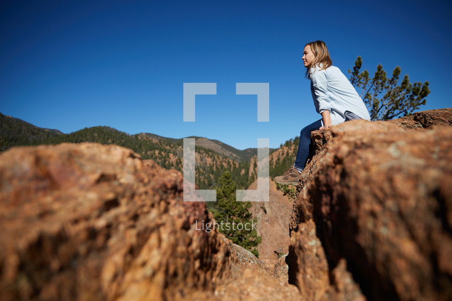 a woman sitting on a red rock with mountain view 