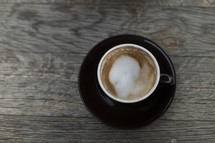 Coffee with foam in black mug on wooden table