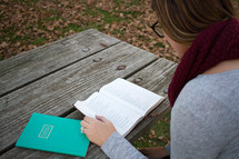 a woman reading a Bible on a picnic table 