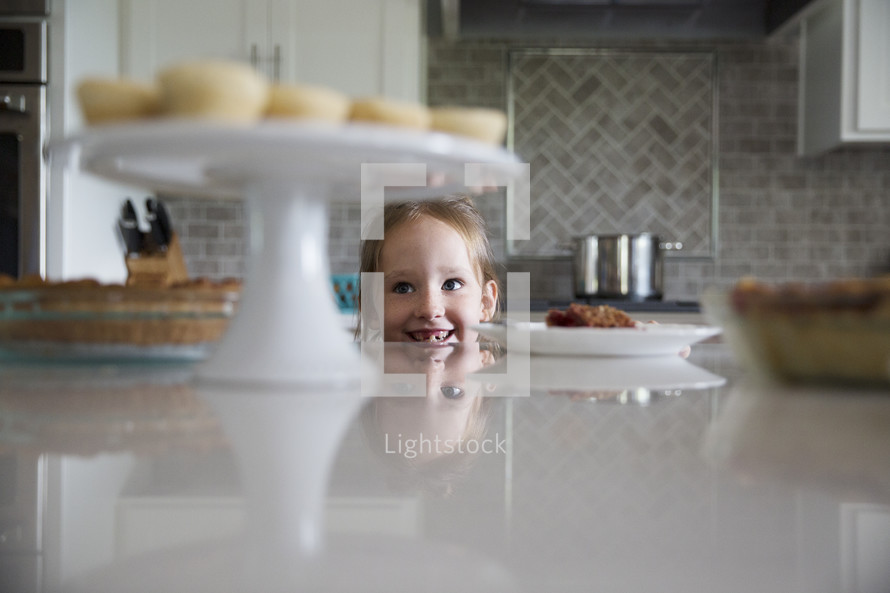 a little girl looking up at dessert on the counter in the kitchen 