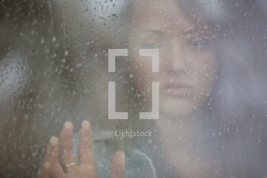 Teenage girl looking out a rainy window pane.