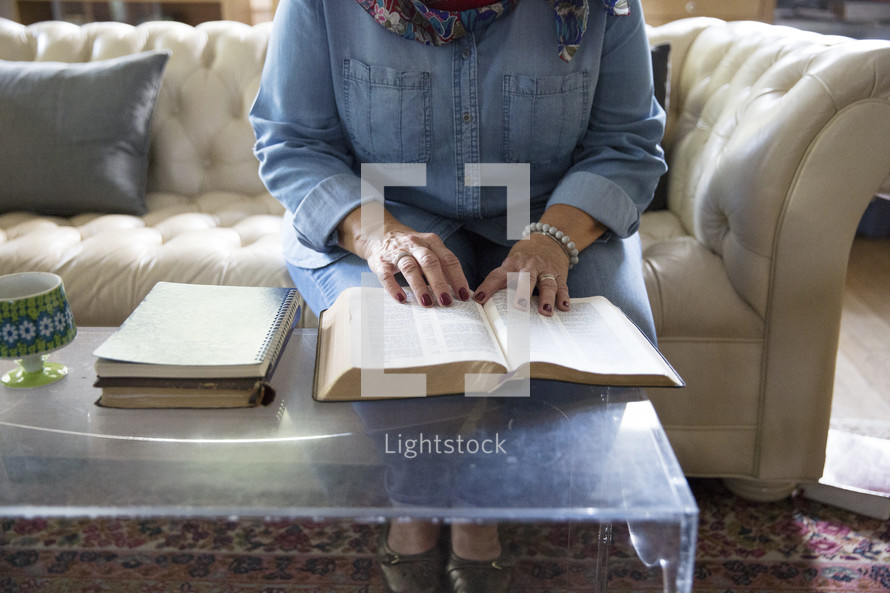 an elderly woman reading a Bible in a living room 