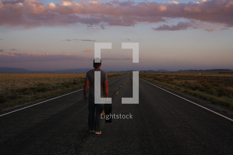 a man standing in the middle of a road with a suitcase at sunset 